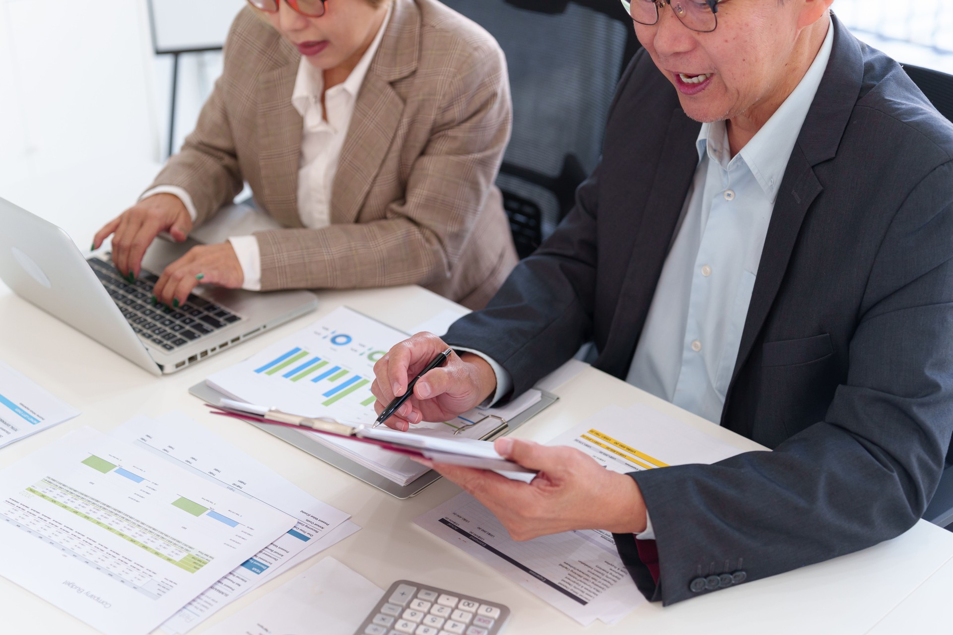 Senior business professionals analyzing financial data together, reviewing reports and discussing investment strategies in a modern office.