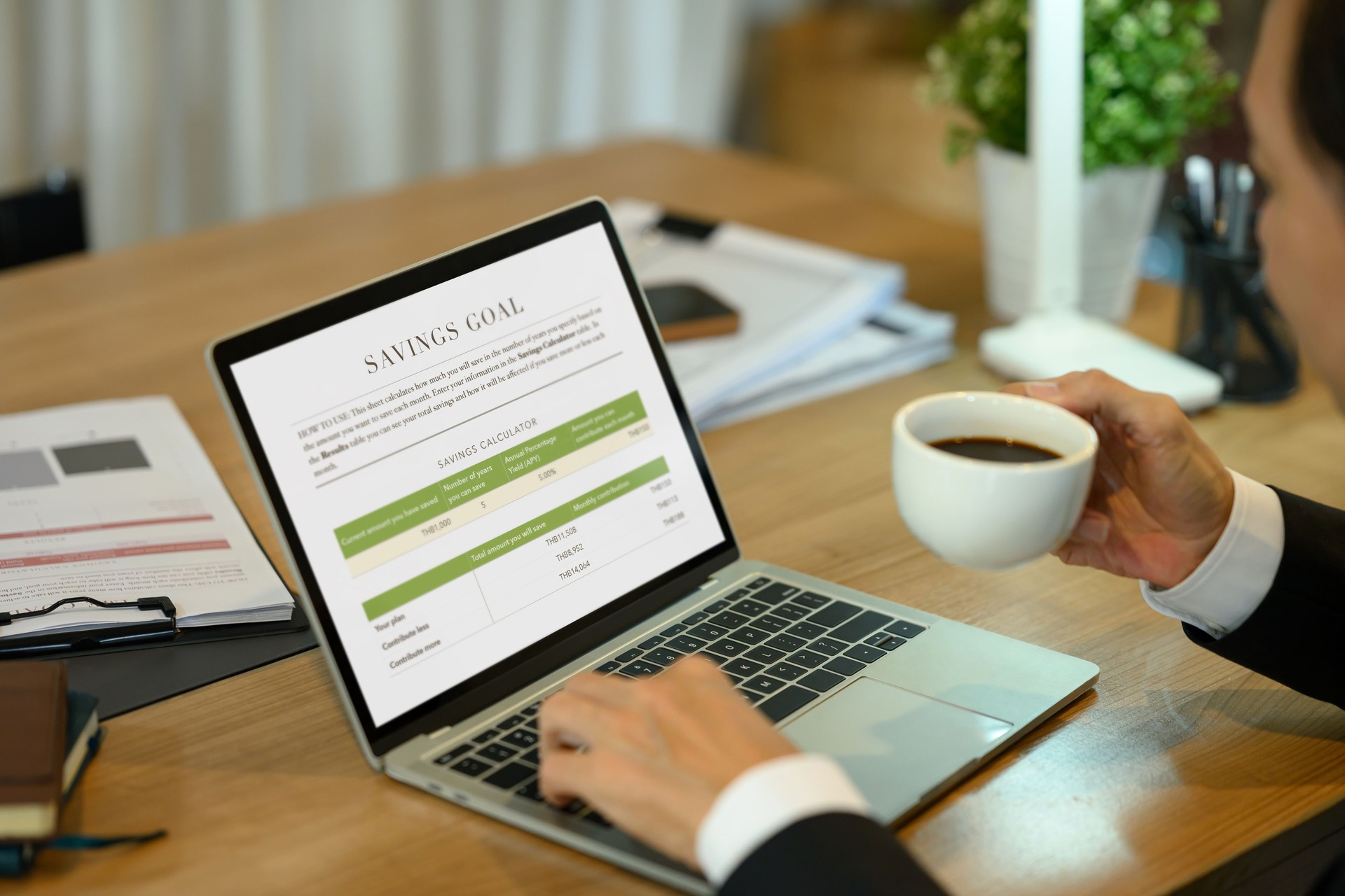 Middle aged businessman holding a cup of coffee using savings goal calculator displayed on laptop screen